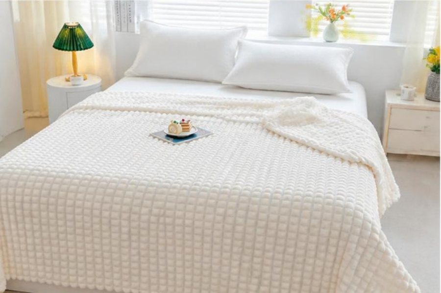 Plaid pour lit blanc à texture gaufrée, posé sur le lit avec des oreillers